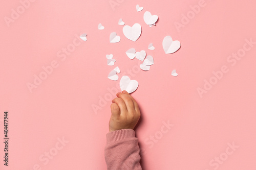 Child's hand takes a valentine card from paper on a pink background. Composition Valentine's Day. Banner. Flat lay, top view