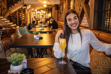Woman in a Restaurant Drinking Lemonade Citrus Fruit Juice. Gorgeous young woman drinking cocktail alone in restaurant. Beautiful woman enjoying fresh cocktail