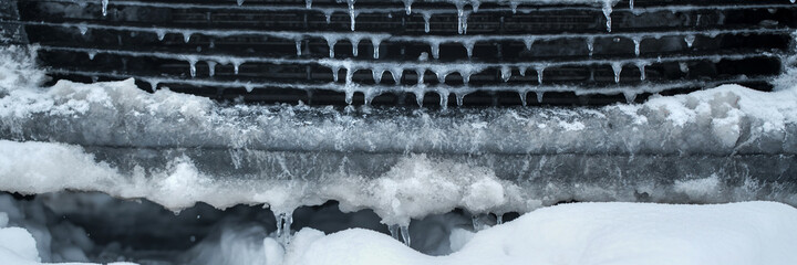 Icy grill of vehicle radiator at city street in winter or spring