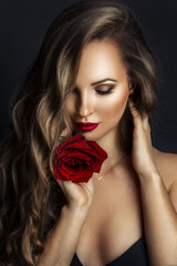 Fashion portrait of young beautiful lady with red rose on black background