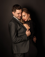 young beautiful couple in black outfits are hugging on a black background.
