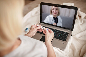 Old woman in bed looking at screen of laptop and consulting with a doctor online at home, telehealth services during lockdown, distant video call, modern tech healthcare application