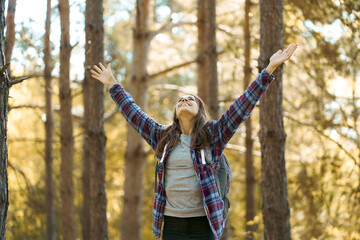 Delighted positive woman with raised hands enjoying beautiful nature in forest. Concept vacations outdoor harmony with nature