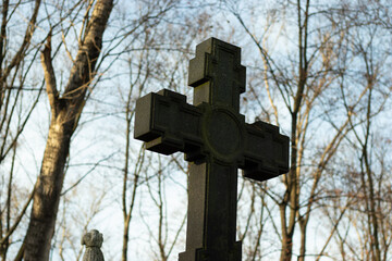 Large Christian cross made of dark stone against the background of tree branches and sky. Religion concept