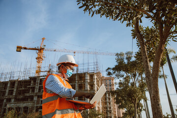 Engineer construction wearing protective mask the spread of Covid 19 diseases during the inspection in construction site with computer laptop. Safety concept