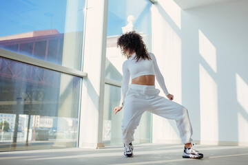Urban style dancer in white clothes doing dance pose. Brunette with big curly hair
