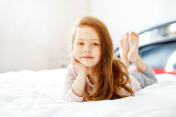 Fototapeta premium Adorable happy little kid girl after sleeping in his white bed in colorful nightwear.