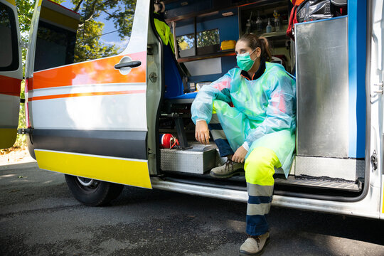 Young woman paramedic rests aboard an ambulance after a first aid intervention during the global pandemic from Covid-19, Coronavirus - Tired and discouraged millennial reflects on the situation