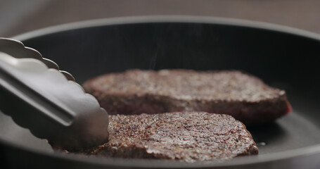 man flipping beef steak on nonstick pan with tongs