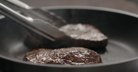 man flipping beef steak on nonstick pan with tongs