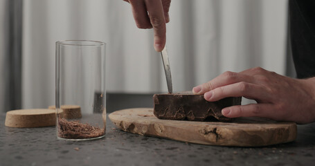 closeup man hands breaking dark chocolate block with knife on wood board