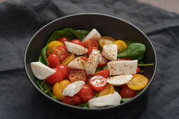 Salad with cherry tomatoes, spinach and mozzarella in black bowl on linen cloth
