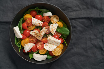 Salad with cherry tomatoes, spinach and mozzarella in black bowl on linen cloth