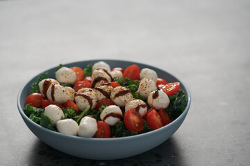 Salad with mozzarella, tomatoes and kale leaves in blue bowl on concrete countertop