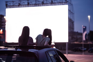 Rear view of two female friends sitting in the car while watching a movie in an open air cinema...