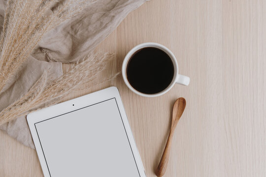 Flatlay female home office desk workspace. Blank screen tablet with copy space. Coffee cup, pampas grass on beige wooden background. Minimalist lifestyle blog mockup. Flat lay, top view.
