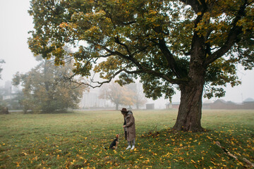 stylish young woman with a dog near a tree in the fog