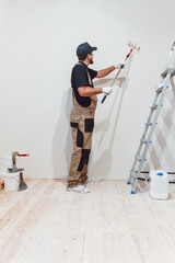 Handsome painter with paint roller in empty room paints the wall