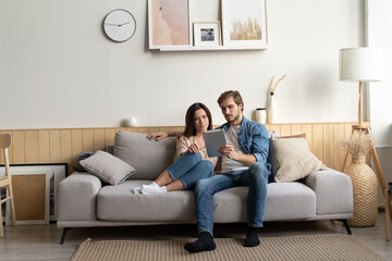 Young couple sitting on couch at home, using a tablet PC for Internet and social media.