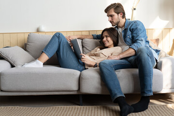 Young couple sitting on couch at home, using a tablet PC for Internet and social media.