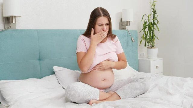Pregnant woman feeling sick with nausesa sitting on bed at morning. Intoxication during pregnancy