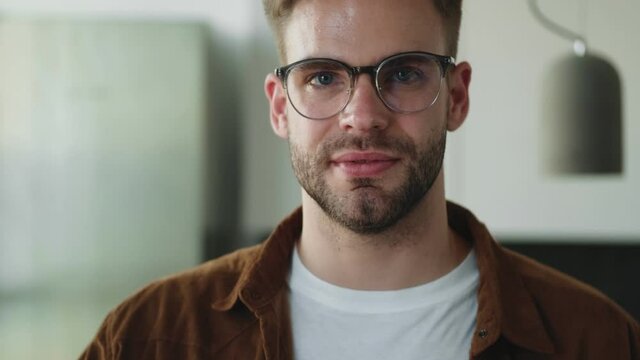 A smiling young man takes-off his eyeglasses sitting at home