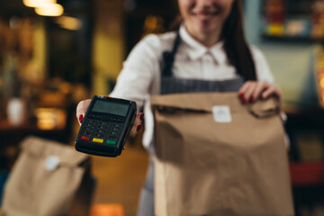woman waitress holding take away food and card payment terminal in restaurant