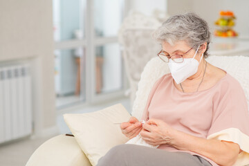 A pretty retired old woman with a medical mask knits at home during a coronavirus lockdown. Ways not to get bored during a lockdown. Quarantine during coronavirus pandemic concept