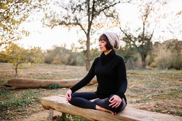 Naklejka na ściany i meble Woman practicing yoga and meditating on the park bench