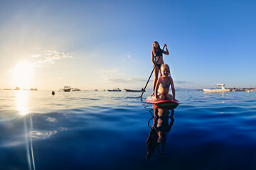 Active paddle boarder at sunset sea. Young mother with little clild paddling on stand up...