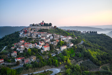 Fototapeta premium Aerial view of the old fortress town located on the mountain. Sunrise. At the foot of the mountain, the morning fog creeps.