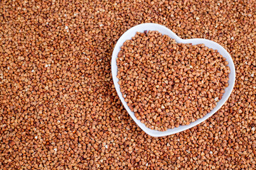 Roasted buckwheat in heart shaped bowl, gluten free ancient grain for healthy eating, selective focus