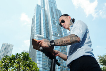 Frowning serious businessman in sunglasses standing near high office building and reading report on tablet computer