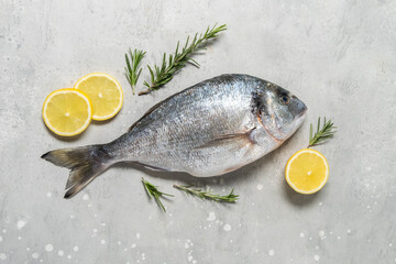 Fresh fish dorado or sea bream  with lemon on stone table with ingredients for cooking  flat lay composition . Healthy food concept. Top view with copy space.