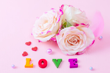 delicate bouquet of bushy peony roses with pearls and feathers and wooden letters Love on a pink background, the concept of congratulations on Valentine's day