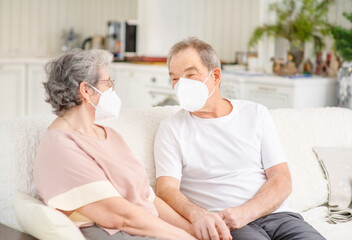 An elderly couple with medical masks sit on the couch at home and chat during a pandemic. Ways not to get bored during lockdown and develop while sitting at home. Quarantine during coronavirus pandemi