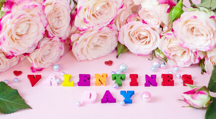 delicate bouquet of bushy peony roses, pearls and wooden colorful letters Valentines day on a pink background
