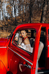 Gorgeous brunette bride posing in red retro car  