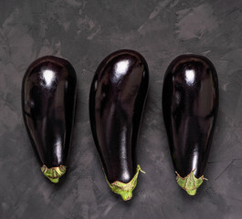 three aubergines on dark textured background