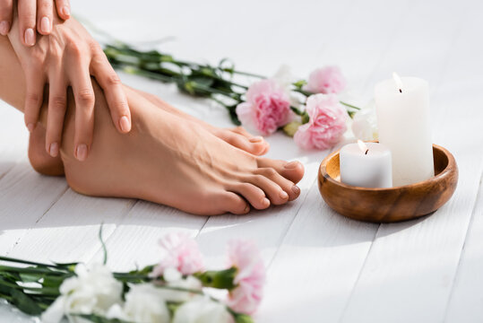 Cropped View Of Woman With Groomed Hands And Feet Near Candles And Flowers On White Wooden Surface, Blurred Foreground