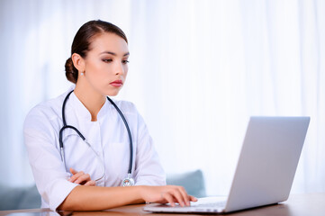 Fototapeta na wymiar Female doctor with stethoscope wearing laboratory coat works in hospital and using laptop