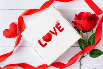 gift box with word Love and red ribbon, heart, flower rose on white wood background, greeting card for Valentines day.