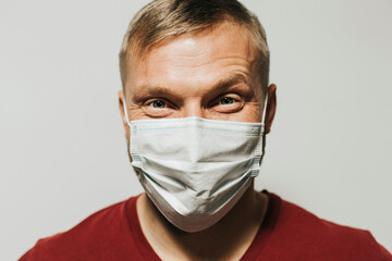 portrait of a smiling man of European appearance in a medical mask on a light background