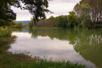 Obraz premium View of the river Ter as it passes through Torello, where the trees that border it are reflected in its calm waters on a summer day. Catalonia, Spain