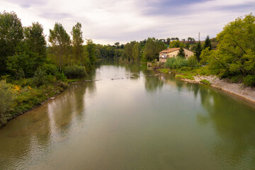 Fototapeta na wymiar View of the river Ter as it passes through Sant Hipolito de Voltrega, where the trees that border it are reflected in its calm waters on a summer day. Catalonia, Spain