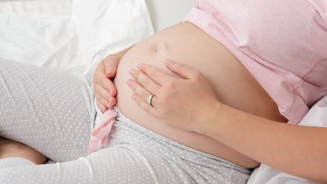 Closeup of beautiful pregnant woman in pajamas lying in bed at morning and stroking her big belly