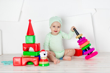 baby plays with toys in the children's room at home in a green bodysuit, the concept of development and leisure of toddlers