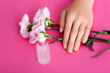 Obraz na płótnie Canvas cropped view of female hand near bottle of cuticle remover and carnation flowers on pink background
