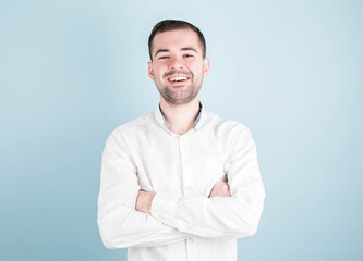 Happy cheerful young brunette businessman, arms crossed, looking at camera with joyful and charming smile.