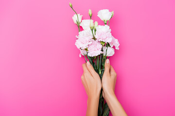 partial view of woman holding carnation and eustoma flowers on pink background